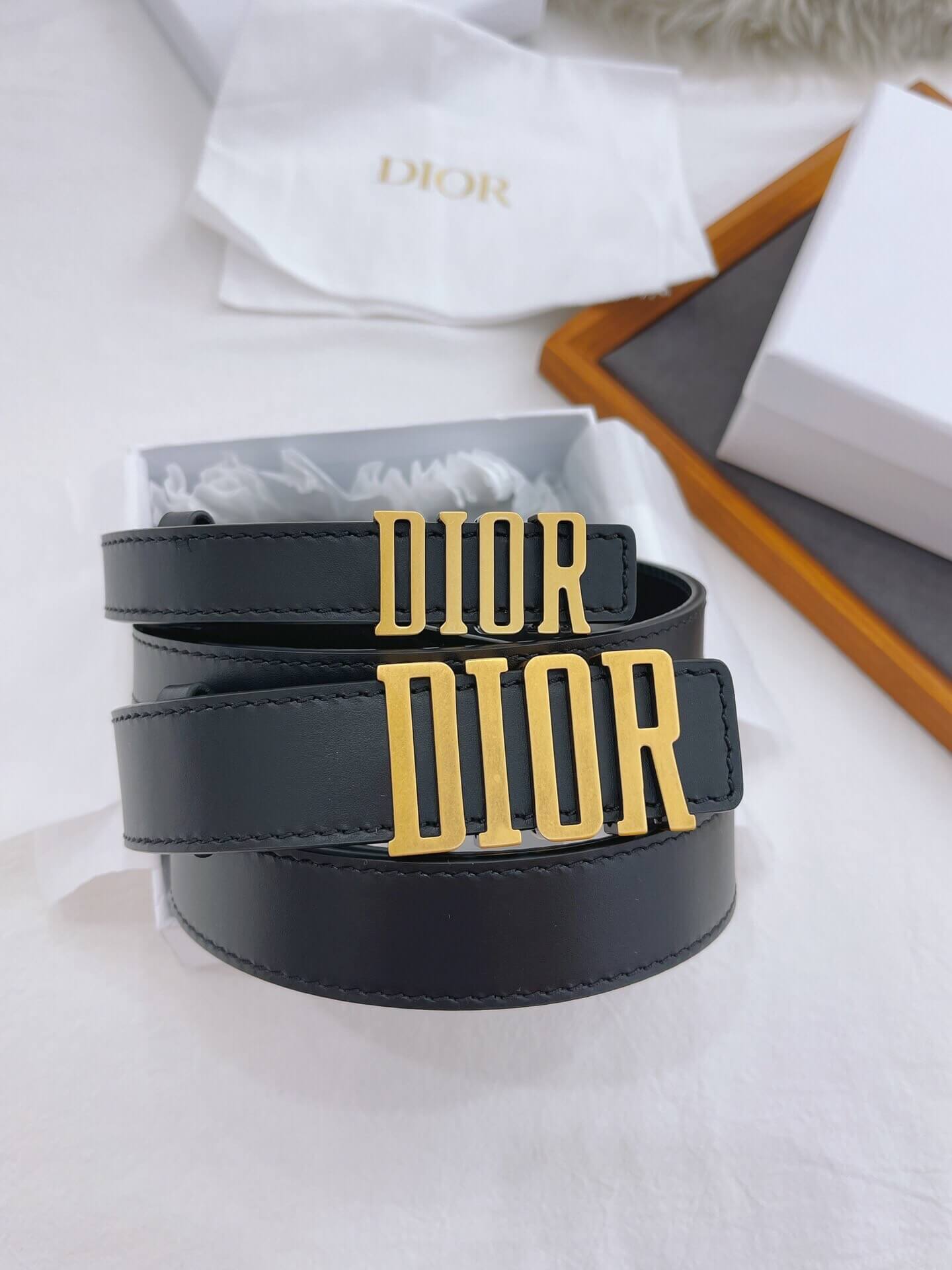 Black Dior belt with gold logo on a white surface