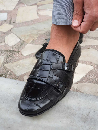 Black Crocodile-Embossed Double Monk Strap Shoe – close-up on foot, highlighting the striking crocodile-embossed leather and sleek double buckles worn with light grey trousers. 