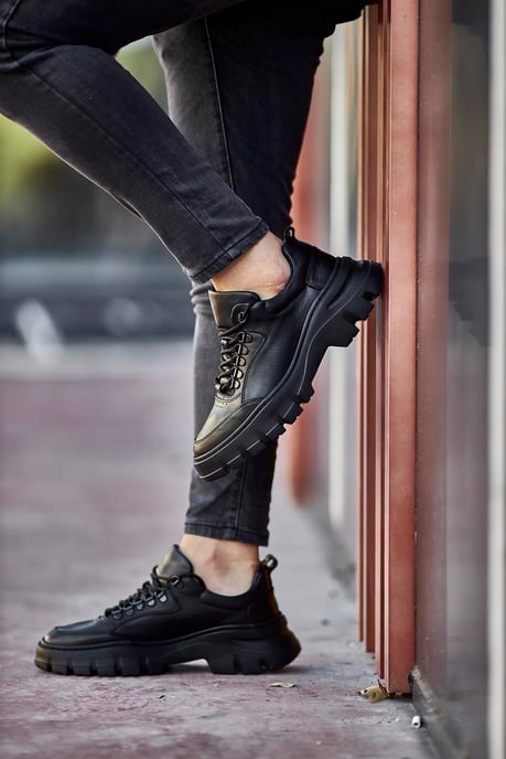 Classic Black Lace Detail Chunky Sneakers - Elegant Leather Footwear for Men – side view, worn by a man in black jeans, leaning against a wall, highlighting the chunky sole and durable construction.