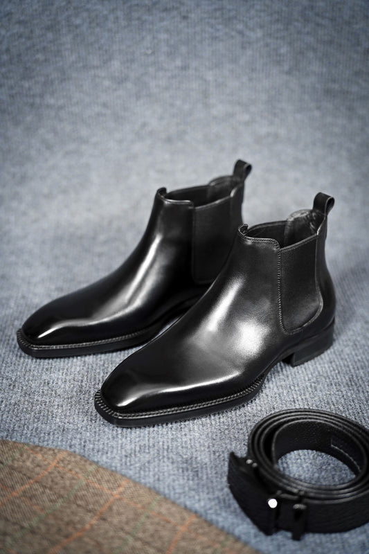 Classic Black Leather Chelsea Boots for Enduring Style – a pair of sleek black leather boots on a textured gray background, showing the full-front view.