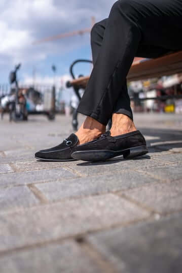 Classic Black Suede Bit Loafers for Office & Evening Wear – worn by a man in black trousers, sitting on a bench, highlighting all-day comfort and a sleek silhouette with metal bit.