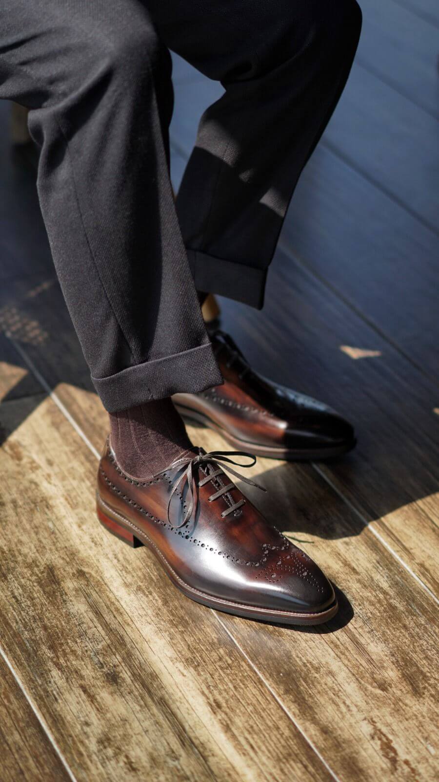 Brown dress shoes on a wooden floor with a person wearing dark pants.
