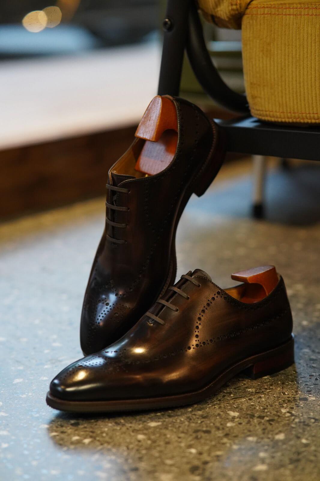 Pair of brown leather dress shoes on a reflective surface with blurred background