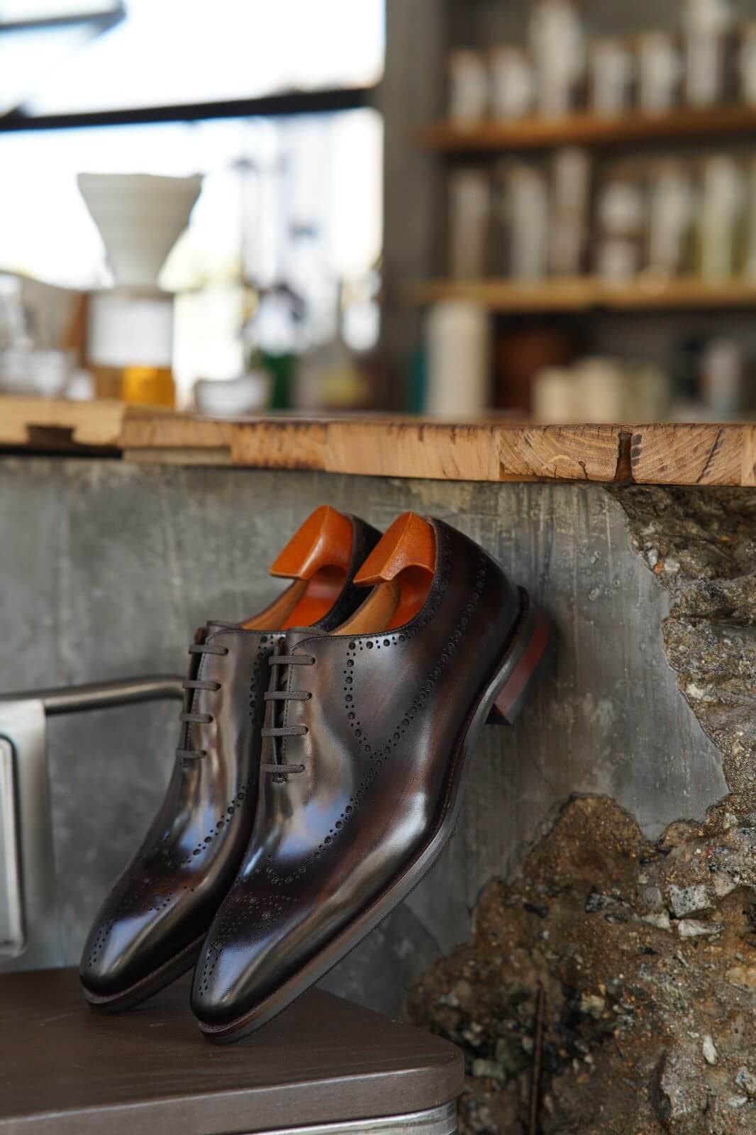 Brown dress shoes with orange soles on a wooden surface, blurred background