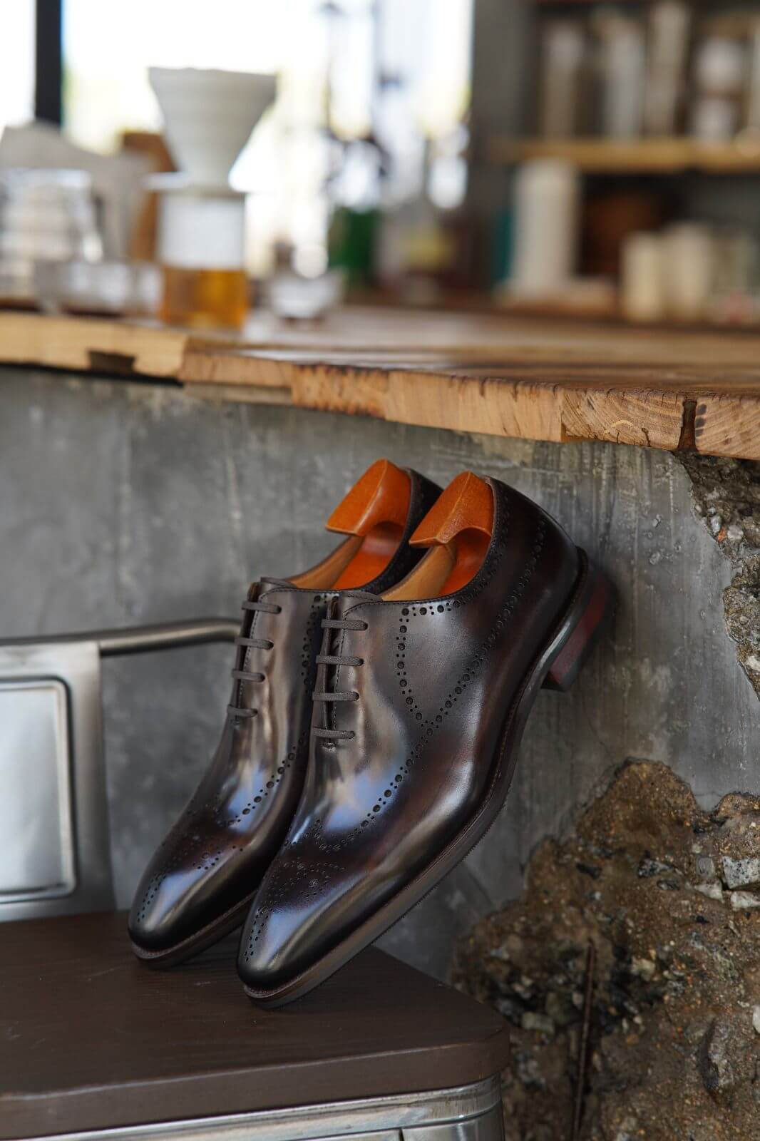 Pair of shiny brown shoes with orange soles on a metal surface.