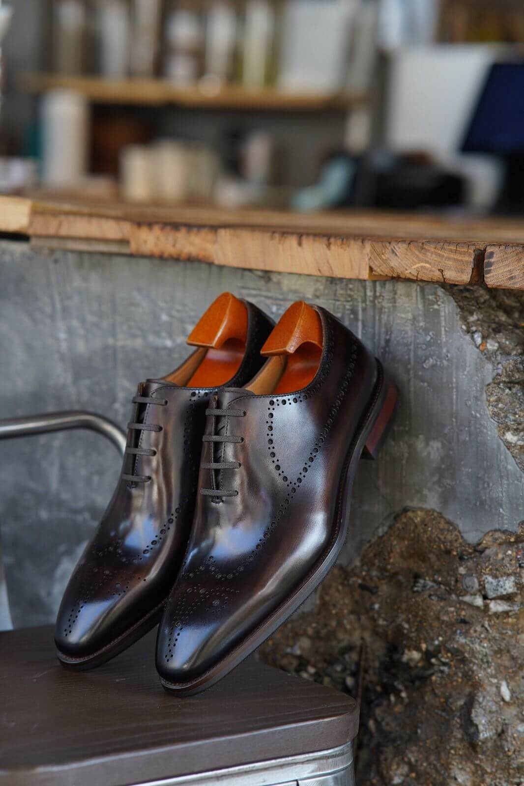 Pair of brown leather shoes with orange soles on a metal surface.