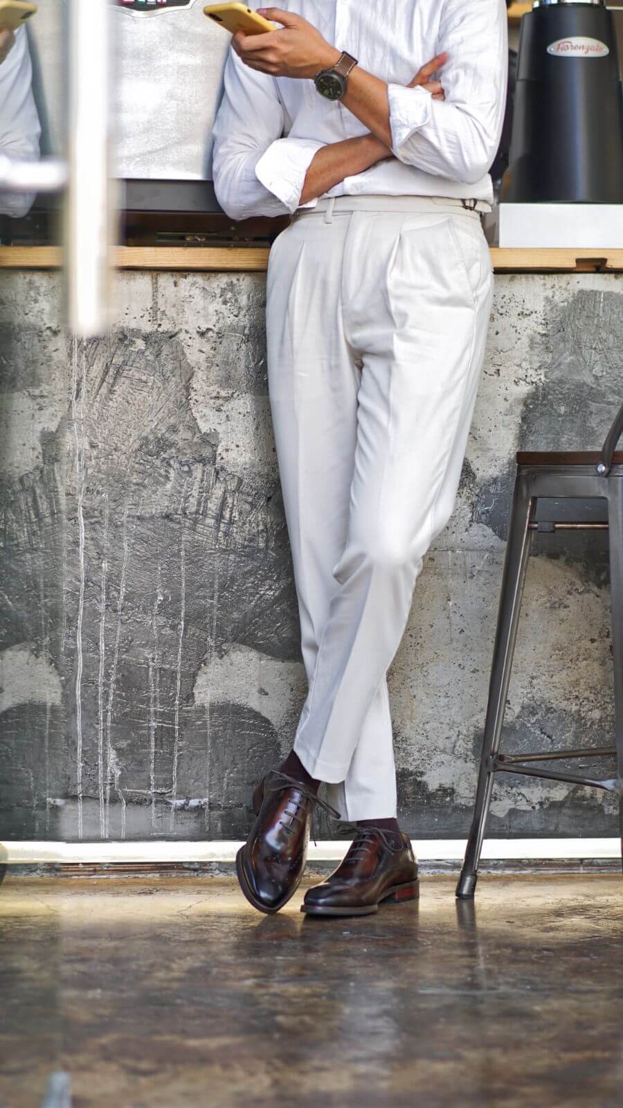 Person wearing a white shirt and light gray pants standing in a room with a textured wall.