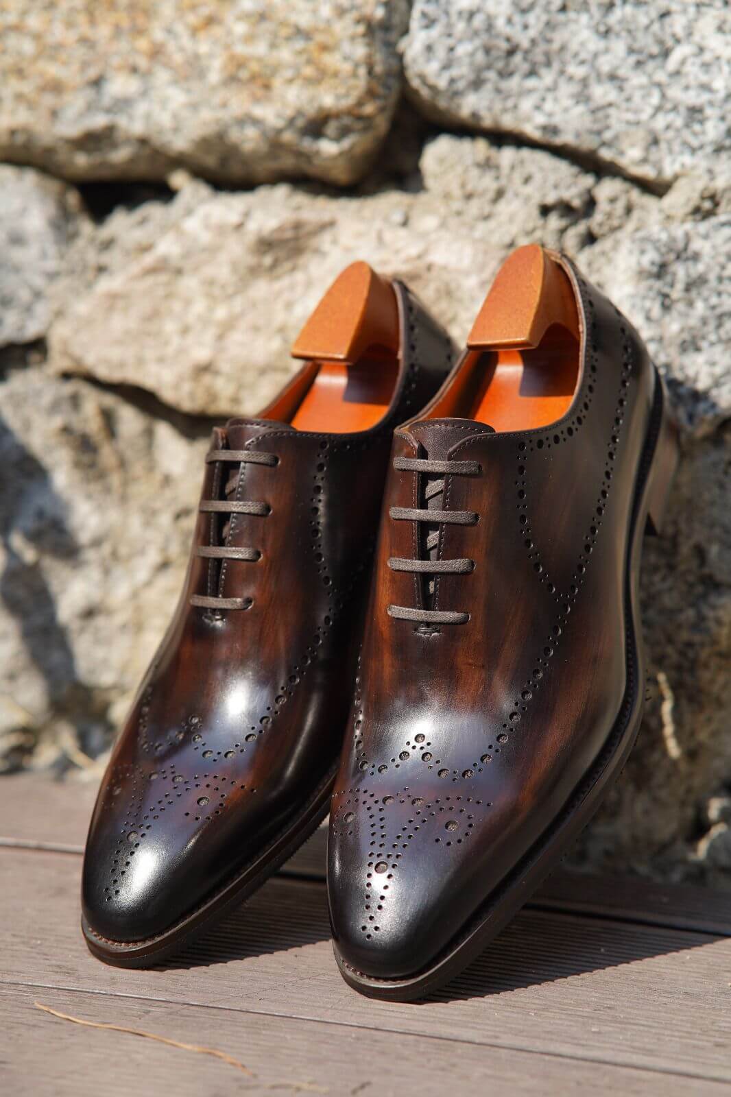 Pair of brown leather dress shoes with orange soles on a stone surface