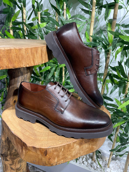 Classic Brown Leather Men's Derby Shoes – premium full-grain leather, displayed on a white ledge with green bamboo and a brick wall background.