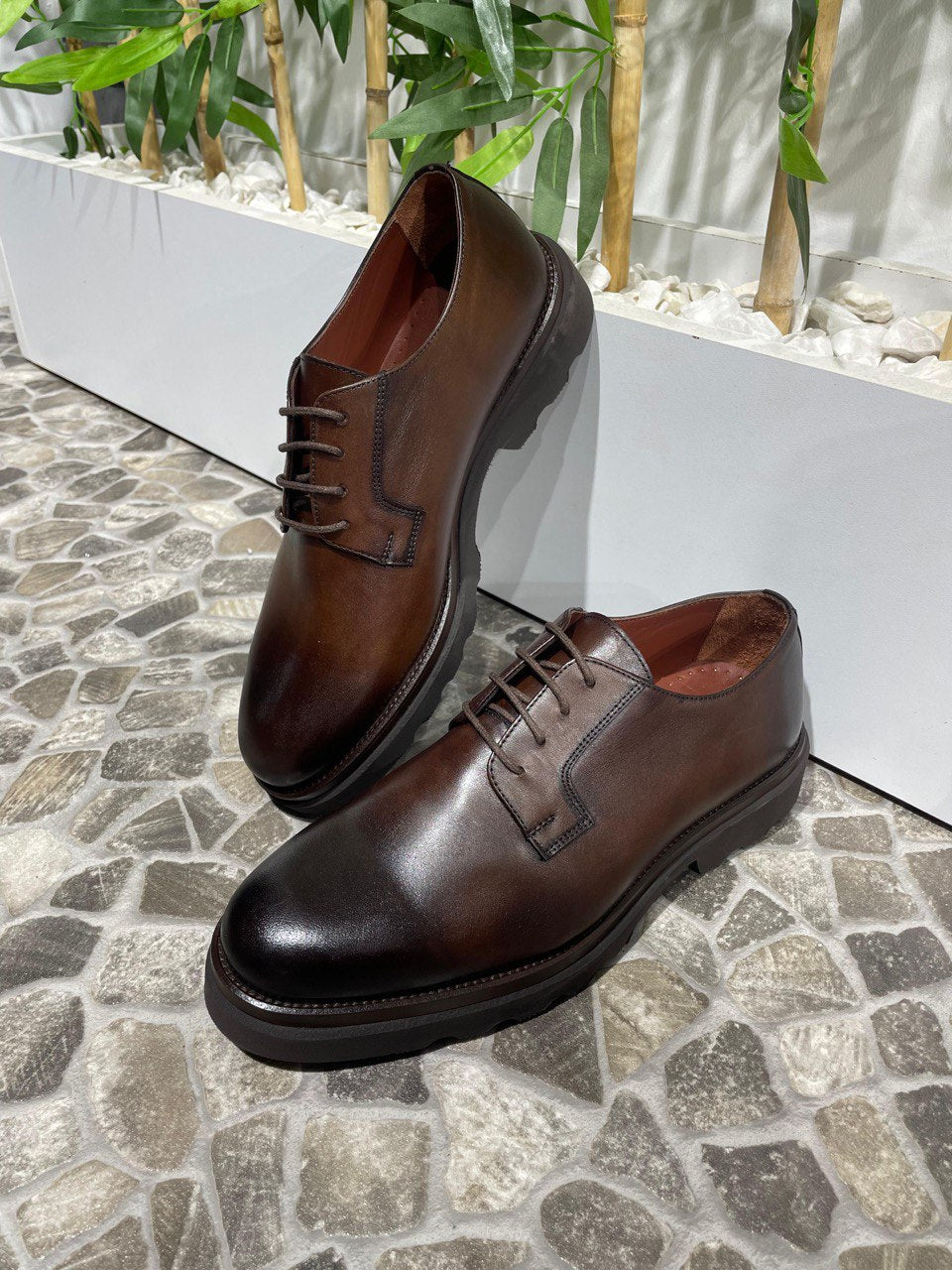 Classic Brown Leather Men's Derby Shoes – elegant brown leather with chunky soles, displayed on a textured stone floor with green plants.