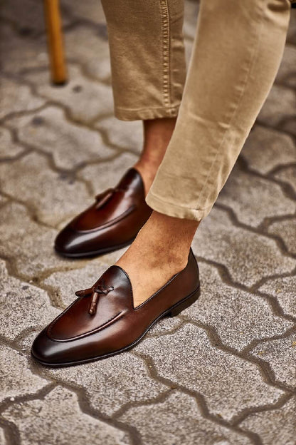 Brown Leather Tassel Loafers for Versatile Style – worn by a man in light cuffed trousers, sitting in a chair, showcasing timeless elegance and sophisticated style.