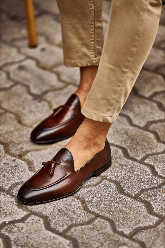Brown Leather Tassel Loafers for Versatile Style – worn by a man in light cuffed trousers, sitting in a chair, showcasing timeless elegance and sophisticated style.