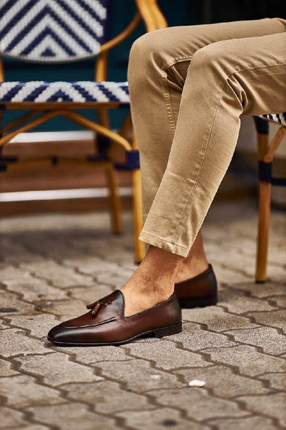 Classic Brown Leather Tassel Loafers for Versatile Style – worn by a man in light cuffed trousers, sitting in a chair, showcasing a timeless design and versatility.