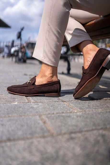 Classic Brown Suede Bit Loafers for Office & Evening Wear – worn by a man in light trousers, sitting on a bench, highlighting all-day comfort and a sleek silhouette with metal bit.
