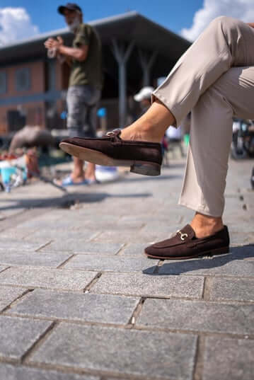 Classic Brown Suede Bit Loafers for Office & Evening Wear – worn by a man in light trousers, with feet on a stone-paved ground, showcasing timeless style and a refined touch with metal bit.