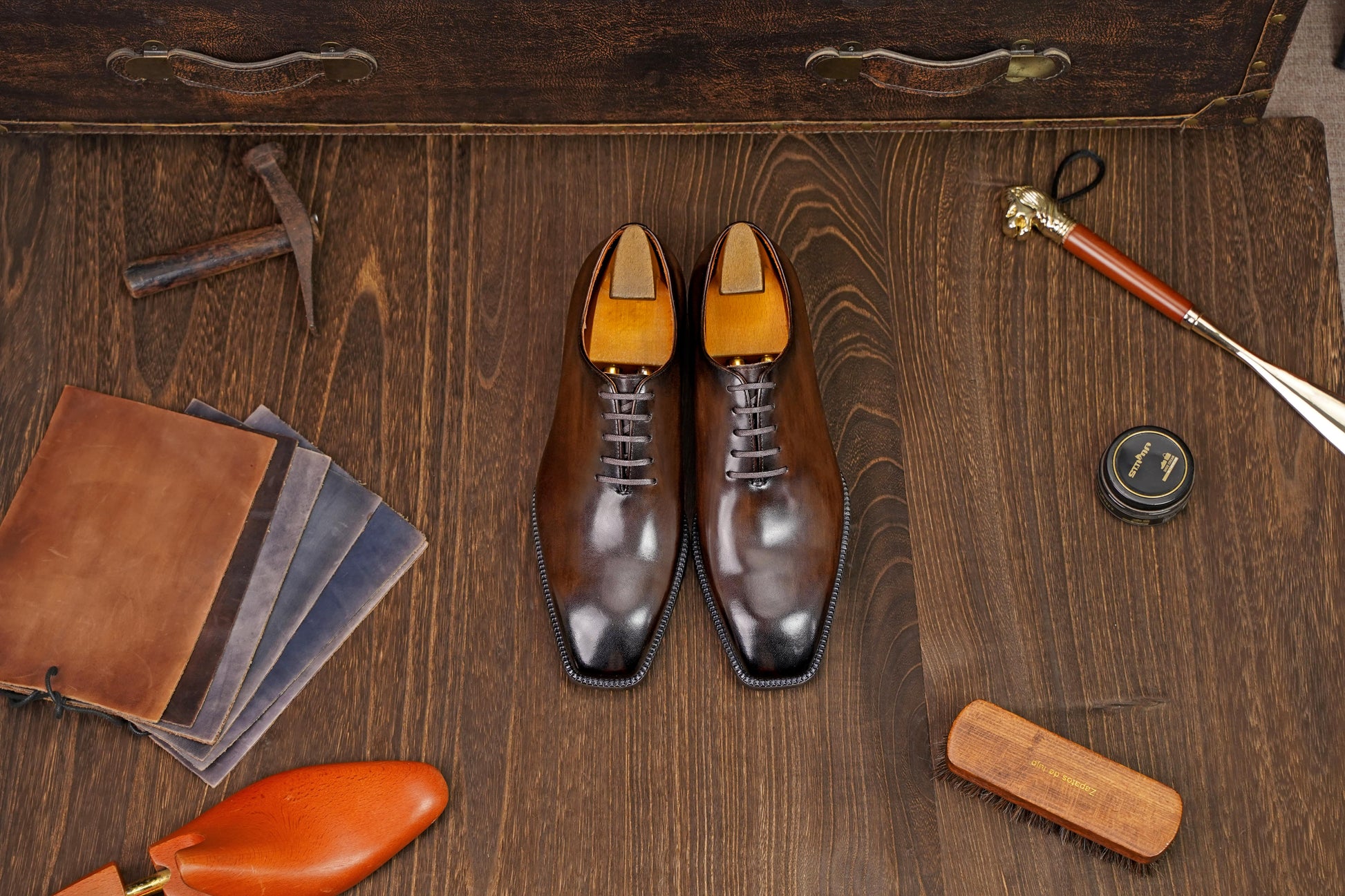 Classic Burnished Brown Leather Wholecut Oxford Dress Shoes – an angled view of the pair of shoes on a wooden surface, surrounded by shoe care accessories and a vintage suitcase.