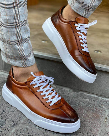 Classic Camel Leather Sneakers for Active Lifestyles & All-Day Wear – worn by a man in plaid trousers, lifting one foot to show the profile, highlighting the chunky white sole and stylish design.