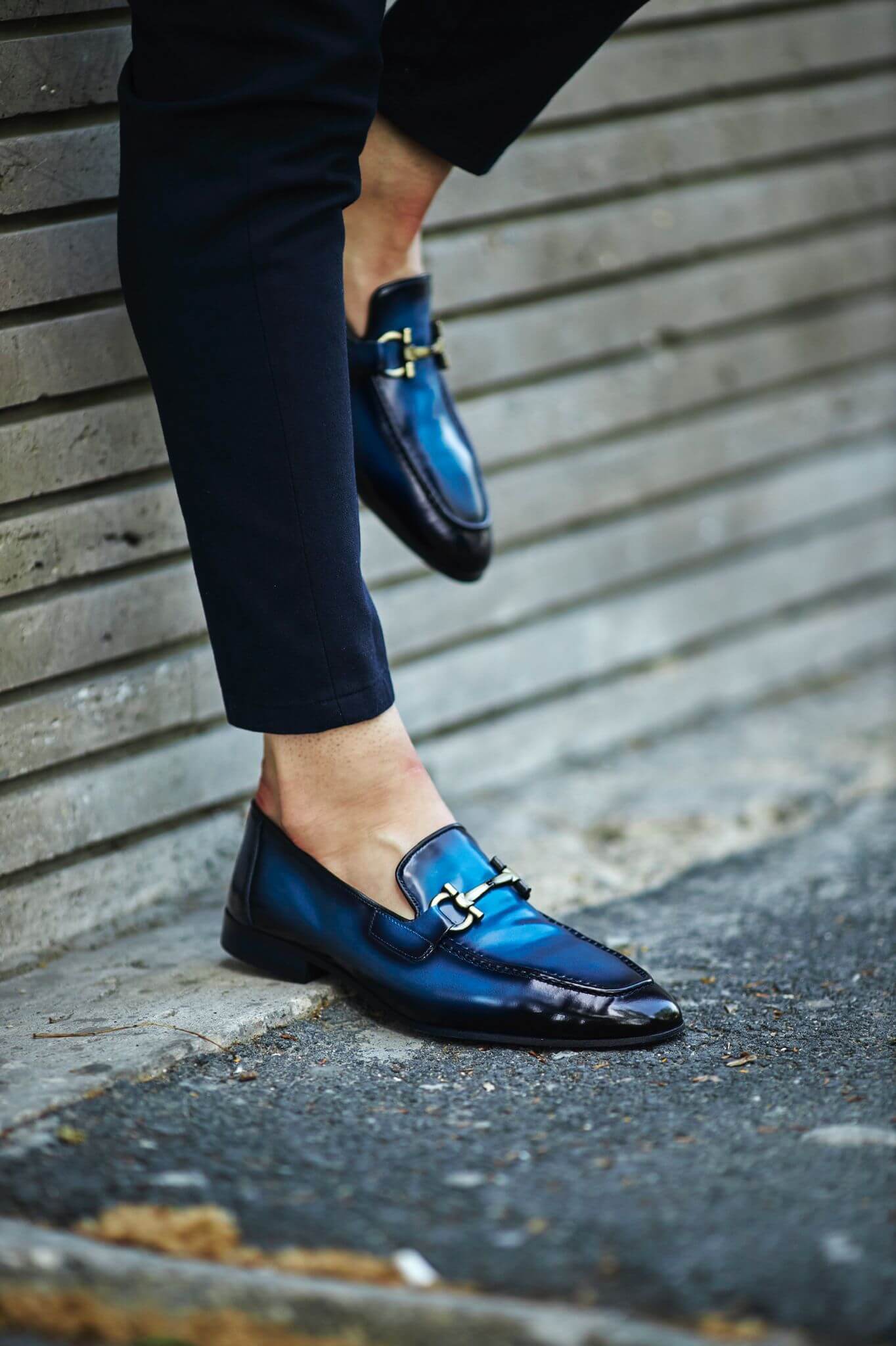Custer Blue Bit Loafers – Classic Leather Footwear for Every Occasion – worn by a man in dark trousers, with one foot lifted, showcasing a classic horsebit buckle and a polished finish.