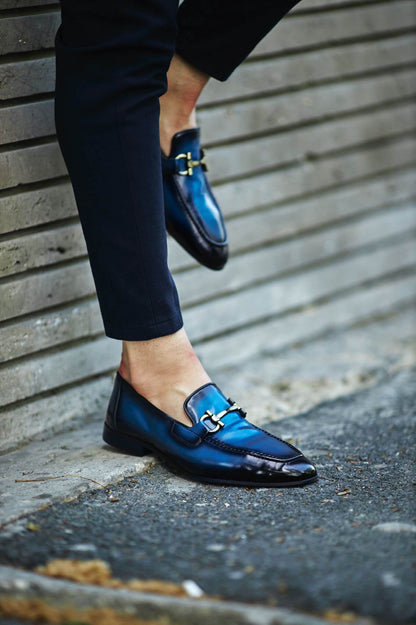 Custer Blue Bit Loafers – Classic Leather Footwear for Every Occasion – worn by a man in dark trousers, with one foot lifted, showcasing a classic horsebit buckle and a polished finish.