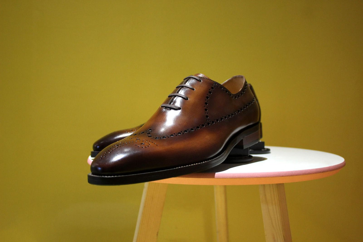 Brown dress shoes on a small stool against a yellow background