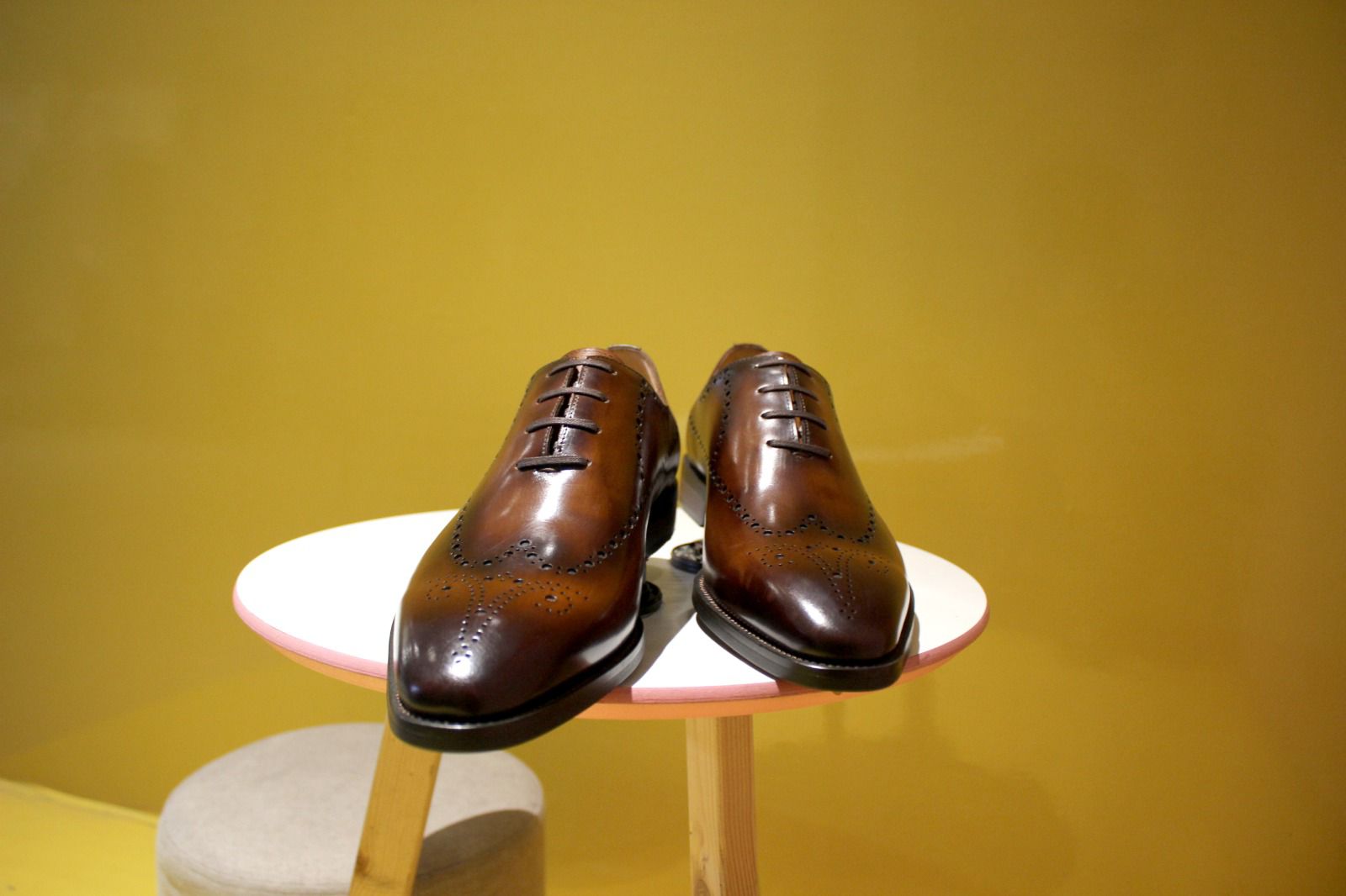 Pair of brown leather shoes on a white stand against a yellow background