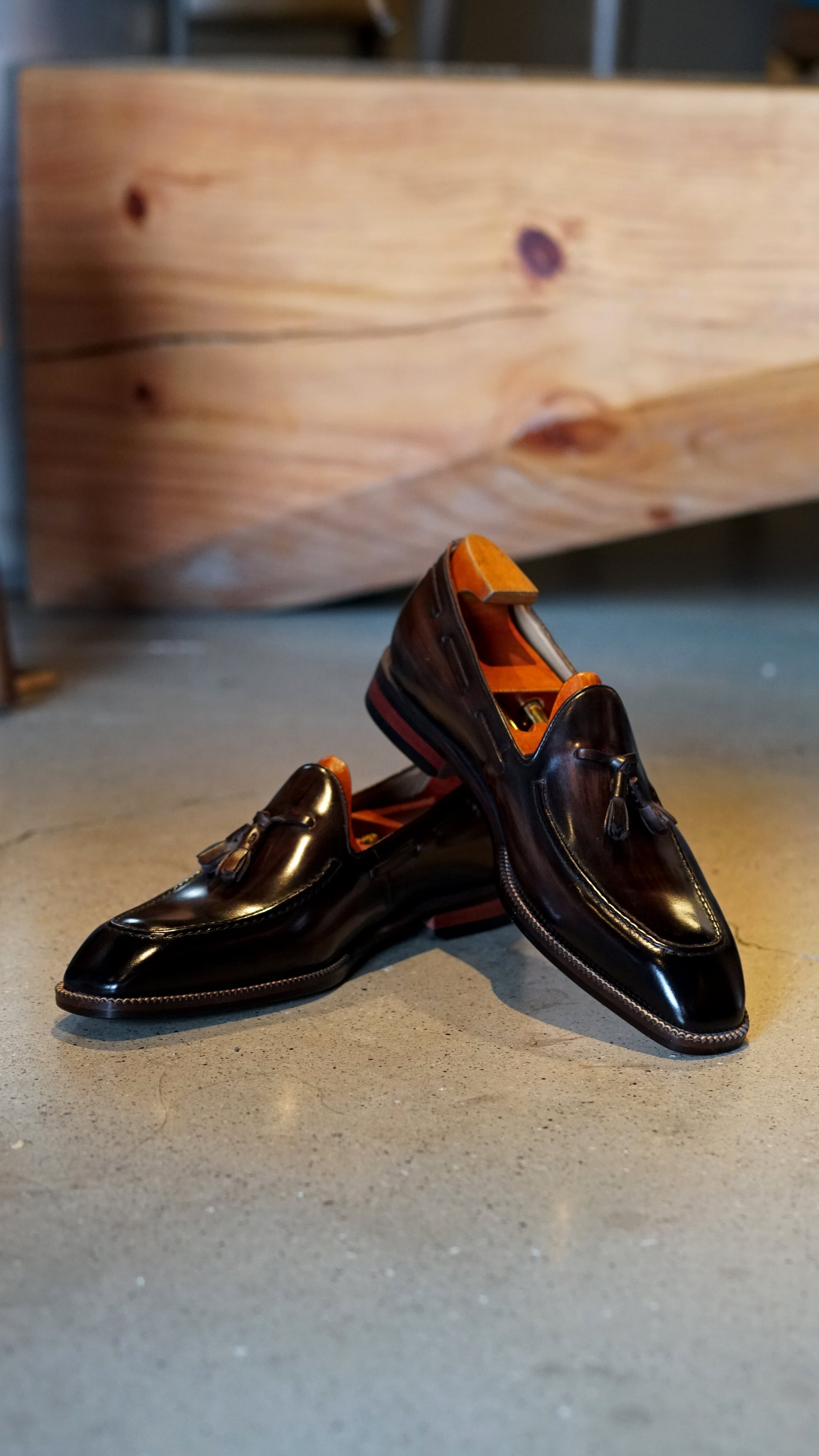 Hand-Made Dark Brown Leather Tassel Loafers – pair with shoe trees, resting on a concrete floor, emphasizing hand-painted patina and rubber grip inserts.