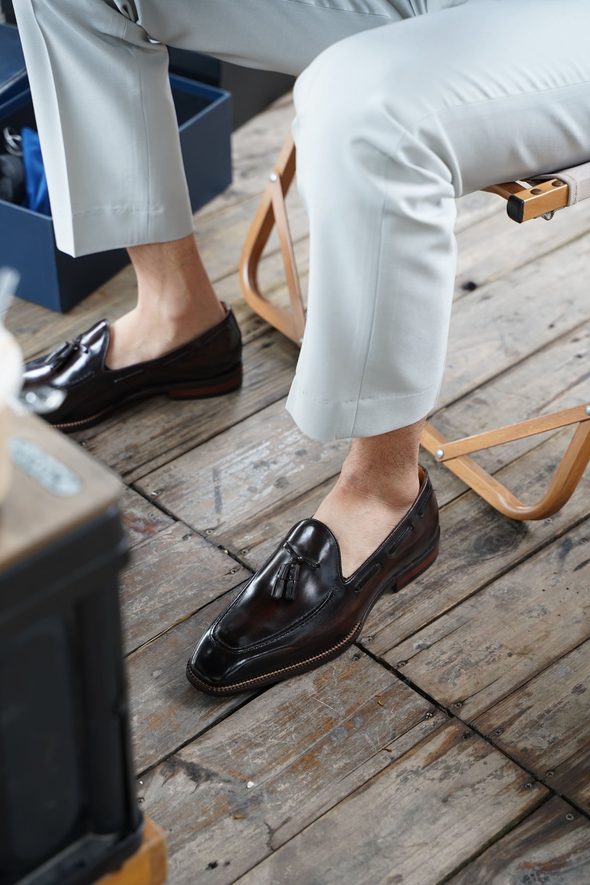 Hand-Made Dark Brown Leather Tassel Loafers – worn by a man in light trousers, sitting on a wooden floor, highlighting the classic tassel and sleek silhouette.