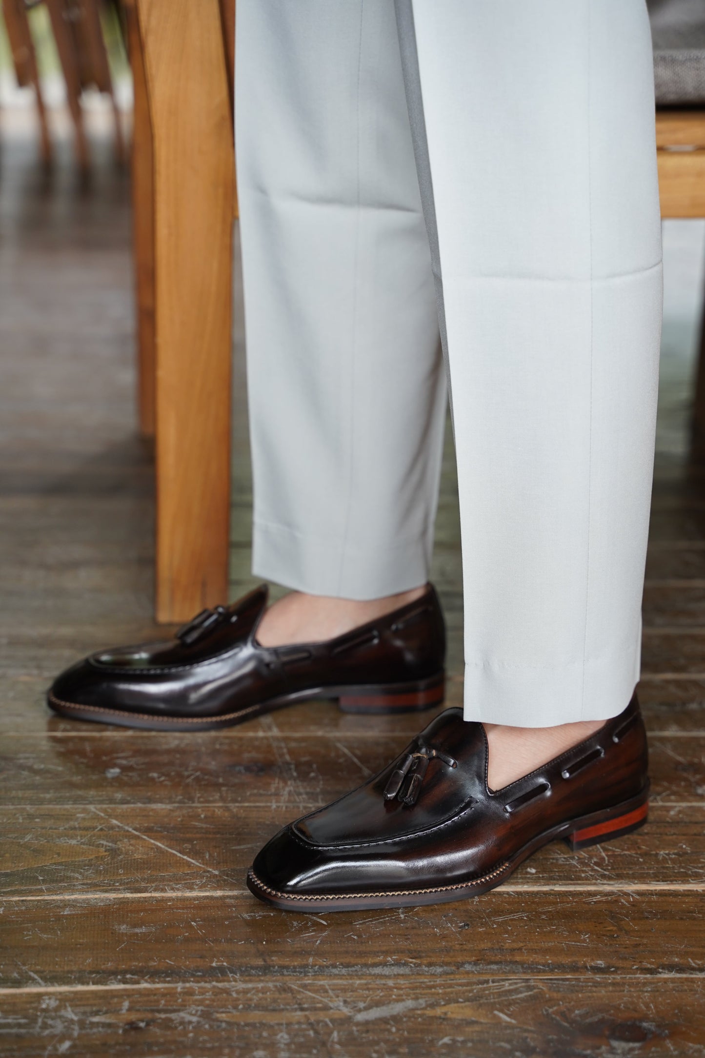 Hand-Made Dark Brown Leather Tassel Loafers – worn by a man in light trousers, showcasing hand-painted patina and sleek almond-toe silhouette on a wooden floor.
