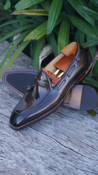 Hand-Made Dark Brown Leather Tassel Loafers – pair with shoe trees on a wooden surface, with green foliage, highlighting sophisticated design.