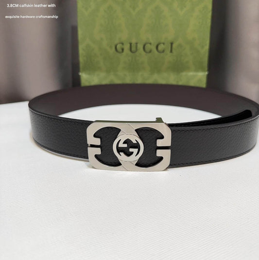 Black Gucci belt with silver buckle on a white surface, with a Gucci box in the background.