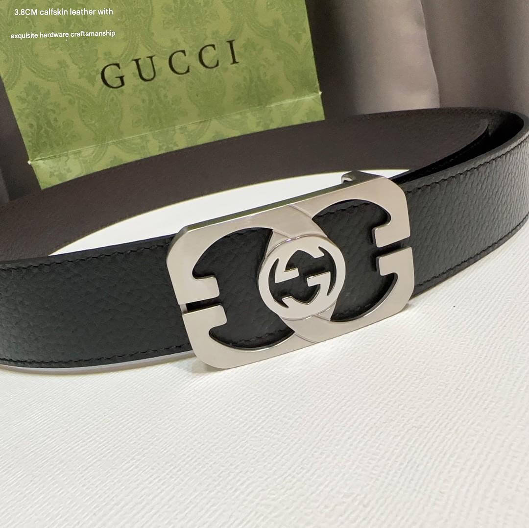 Black Gucci belt with silver buckle on a white surface, with a green box in the background.