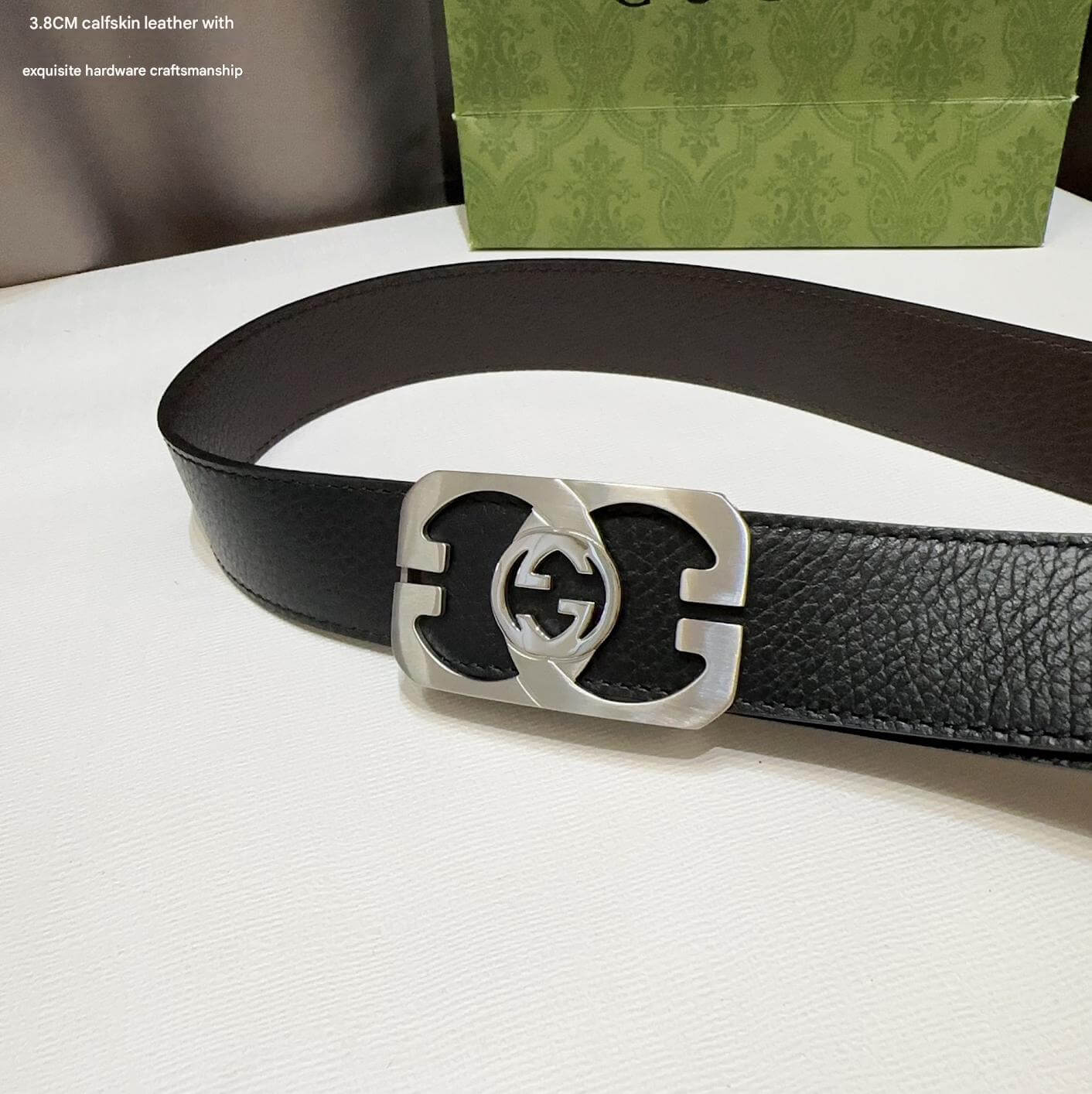 Black leather belt with silver buckle on a white surface, with a green patterned box in the background.