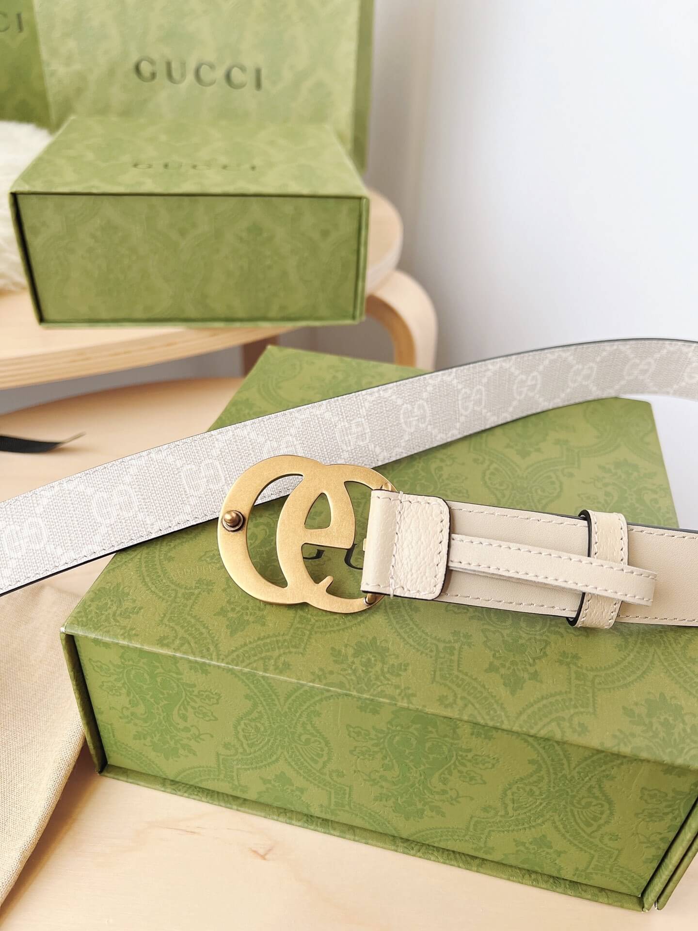 Beige belt with a gold buckle on a green box, Gucci branding visible