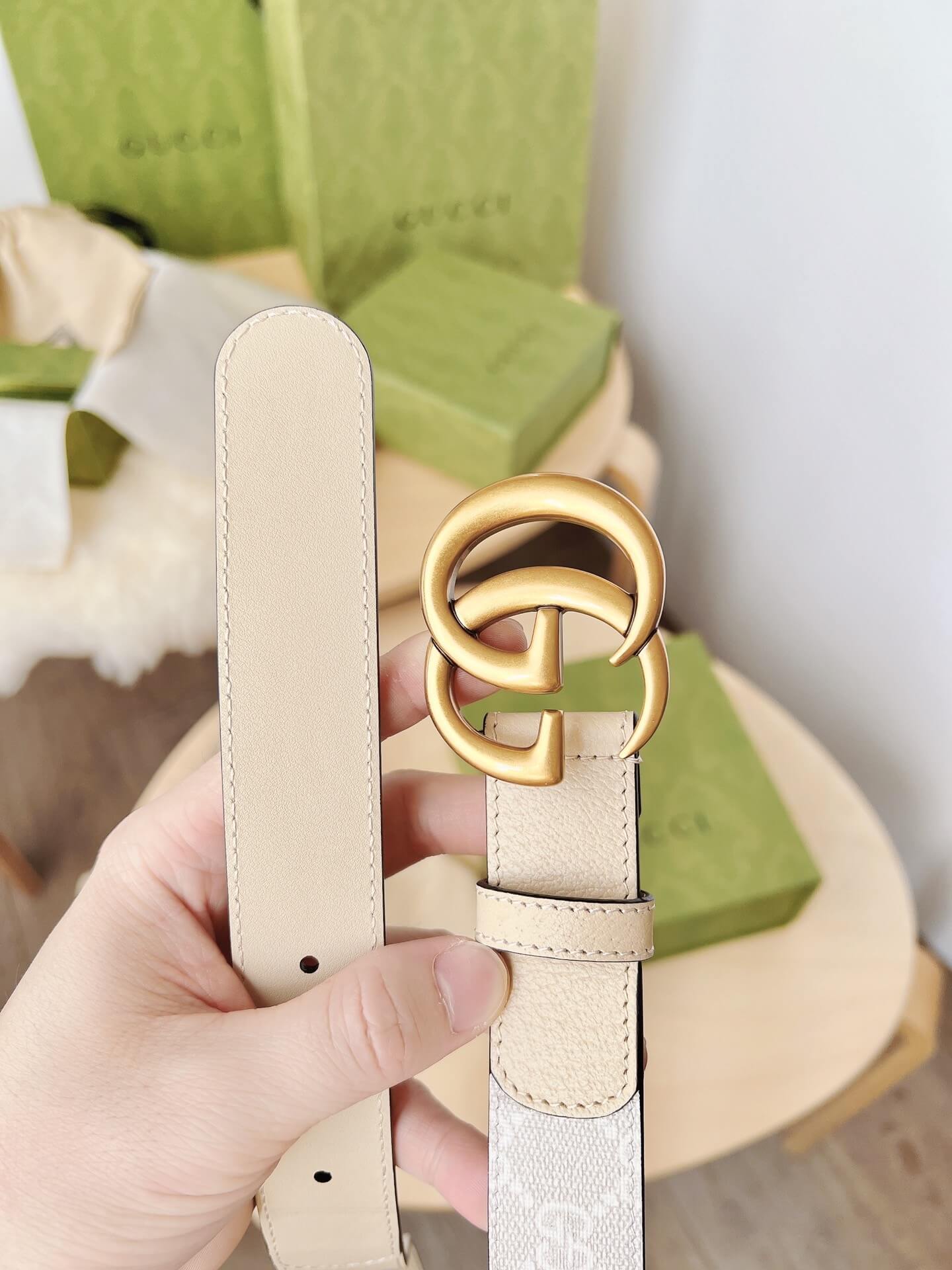 Beige leather belt with gold buckle held by a hand, Gucci box in the background