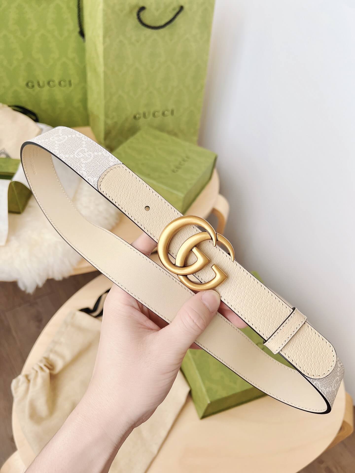 Beige belt with gold logo held by a hand, Gucci box in the background