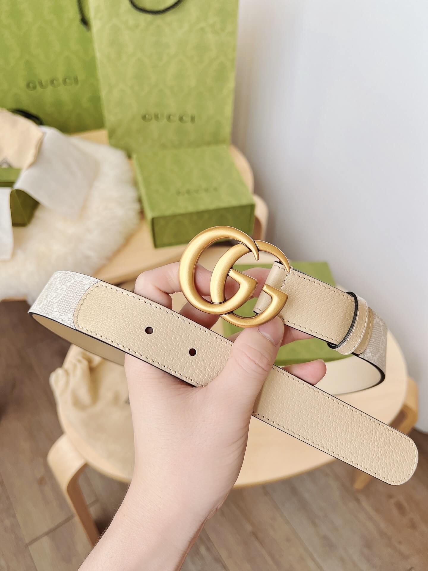 Beige belt with gold ring buckle held by a hand, Gucci box in the background