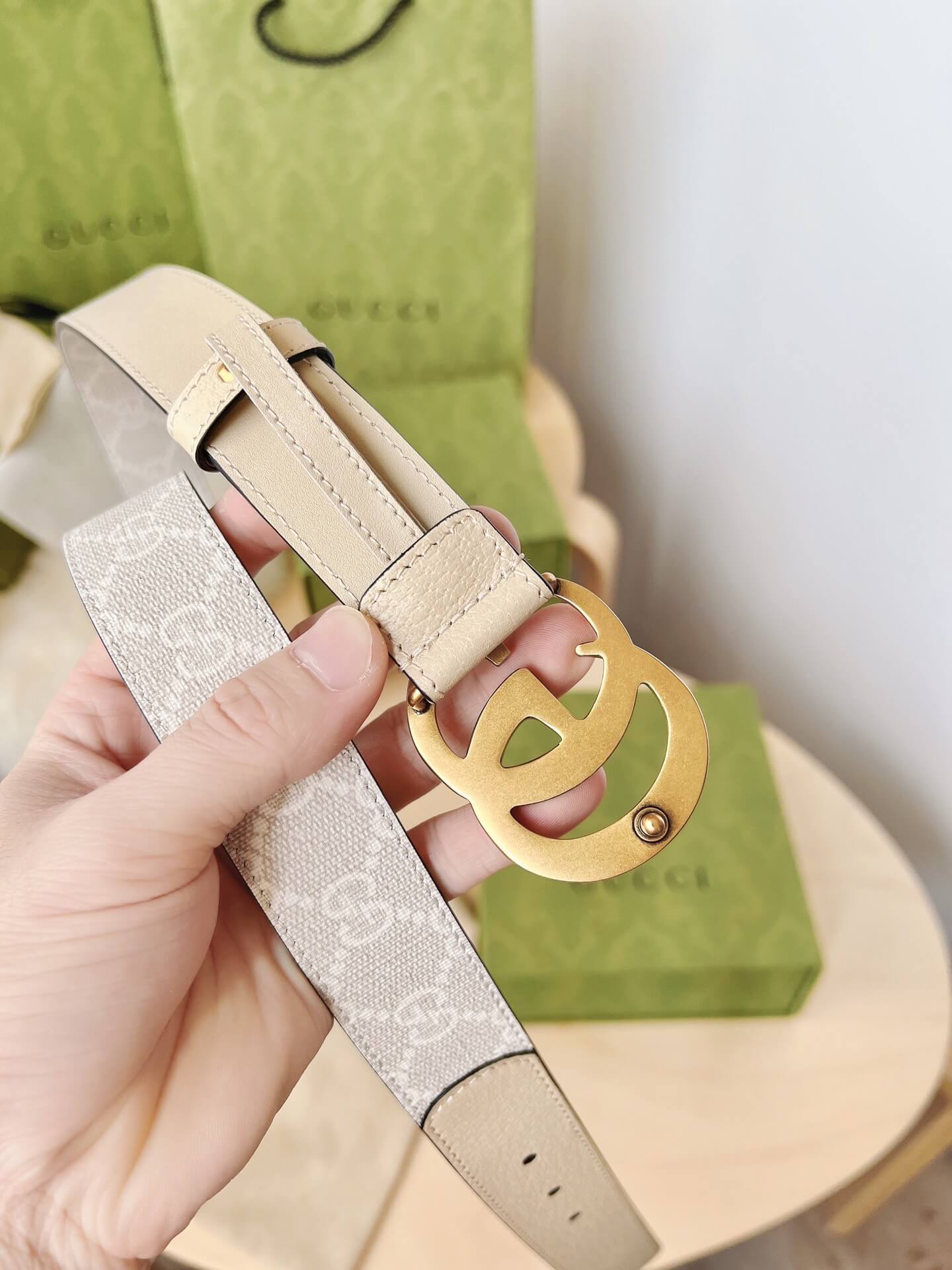 Beige Gucci belt with gold buckle held by a hand, Gucci box in the background