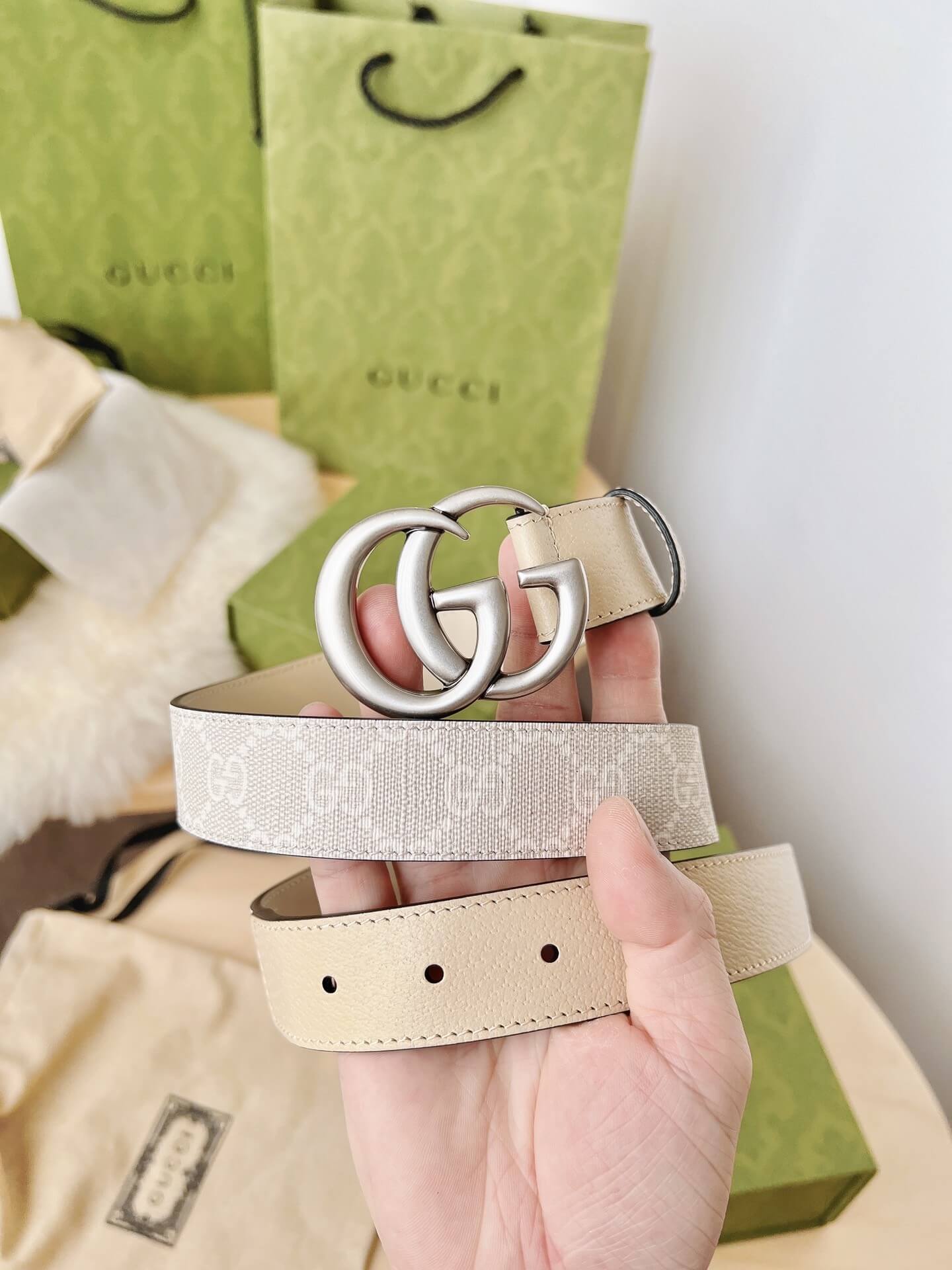Hand holding a Gucci belt with a Gucci bag in the background