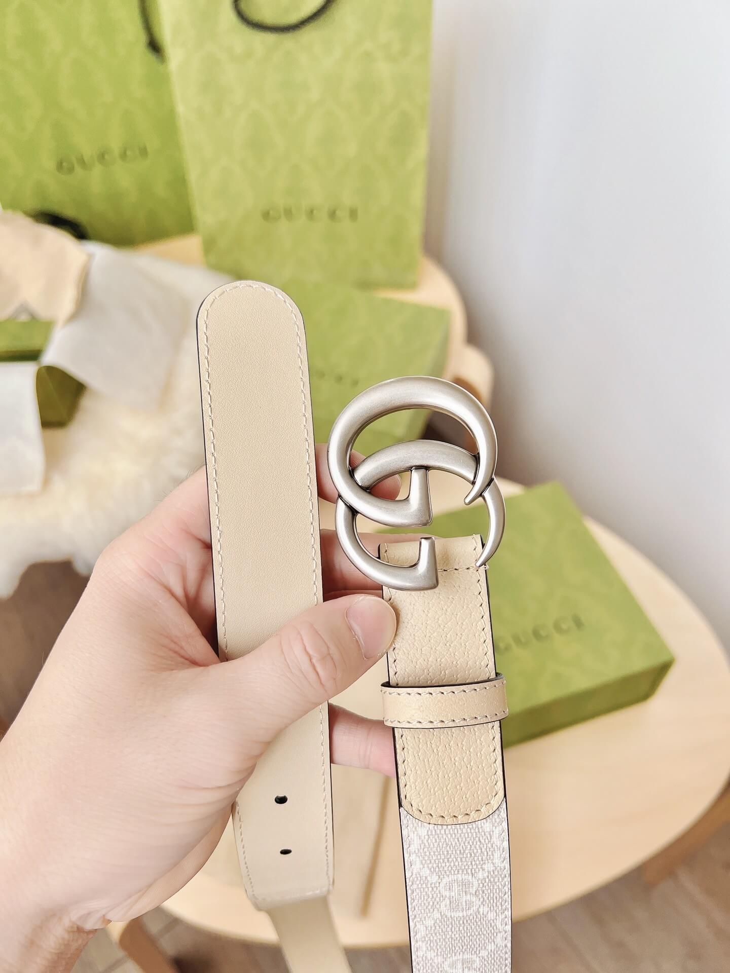 Beige belt with silver buckle held by a hand, Gucci box in the background