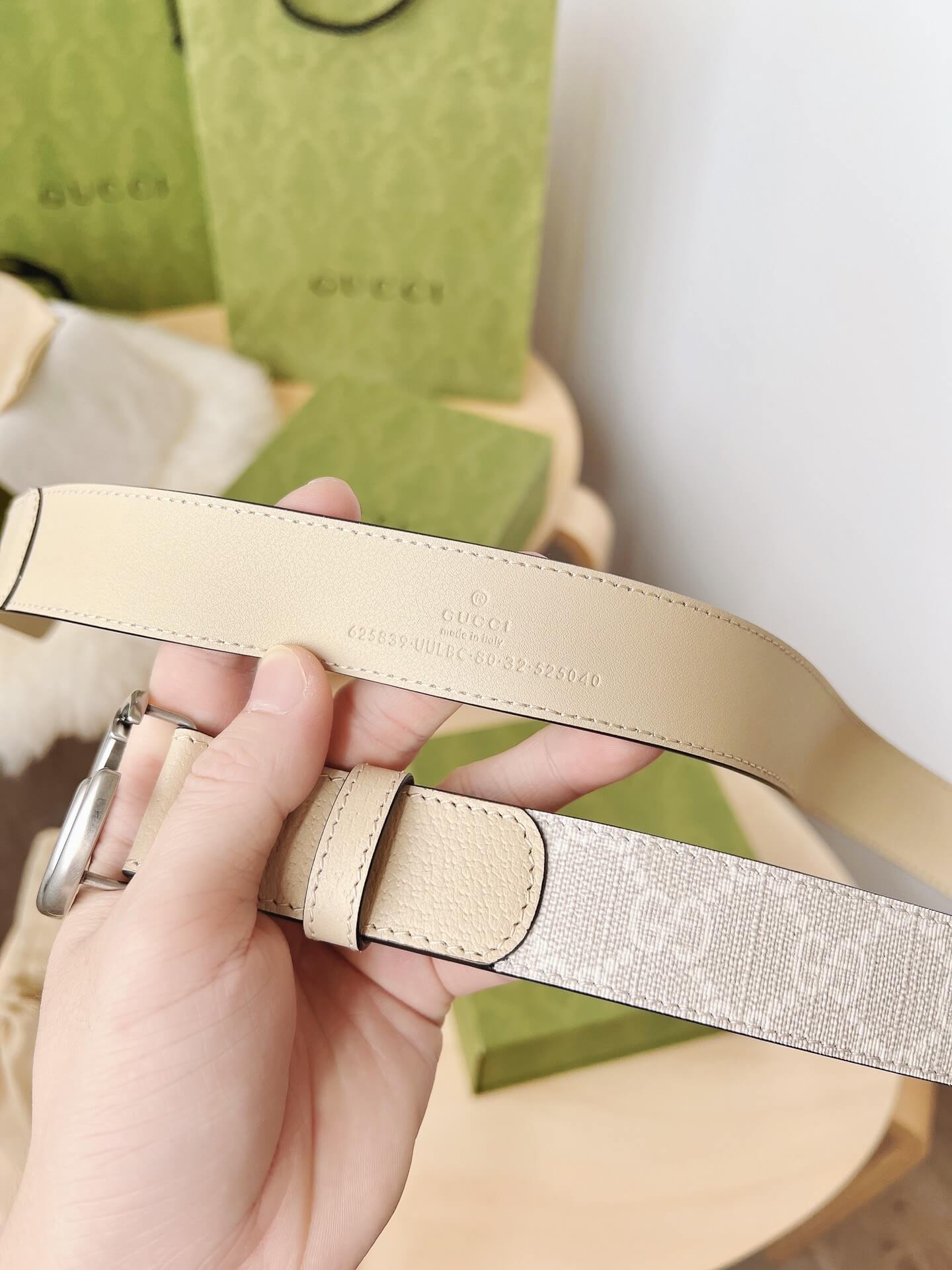 Hand holding a Gucci belt with a Gucci box in the background