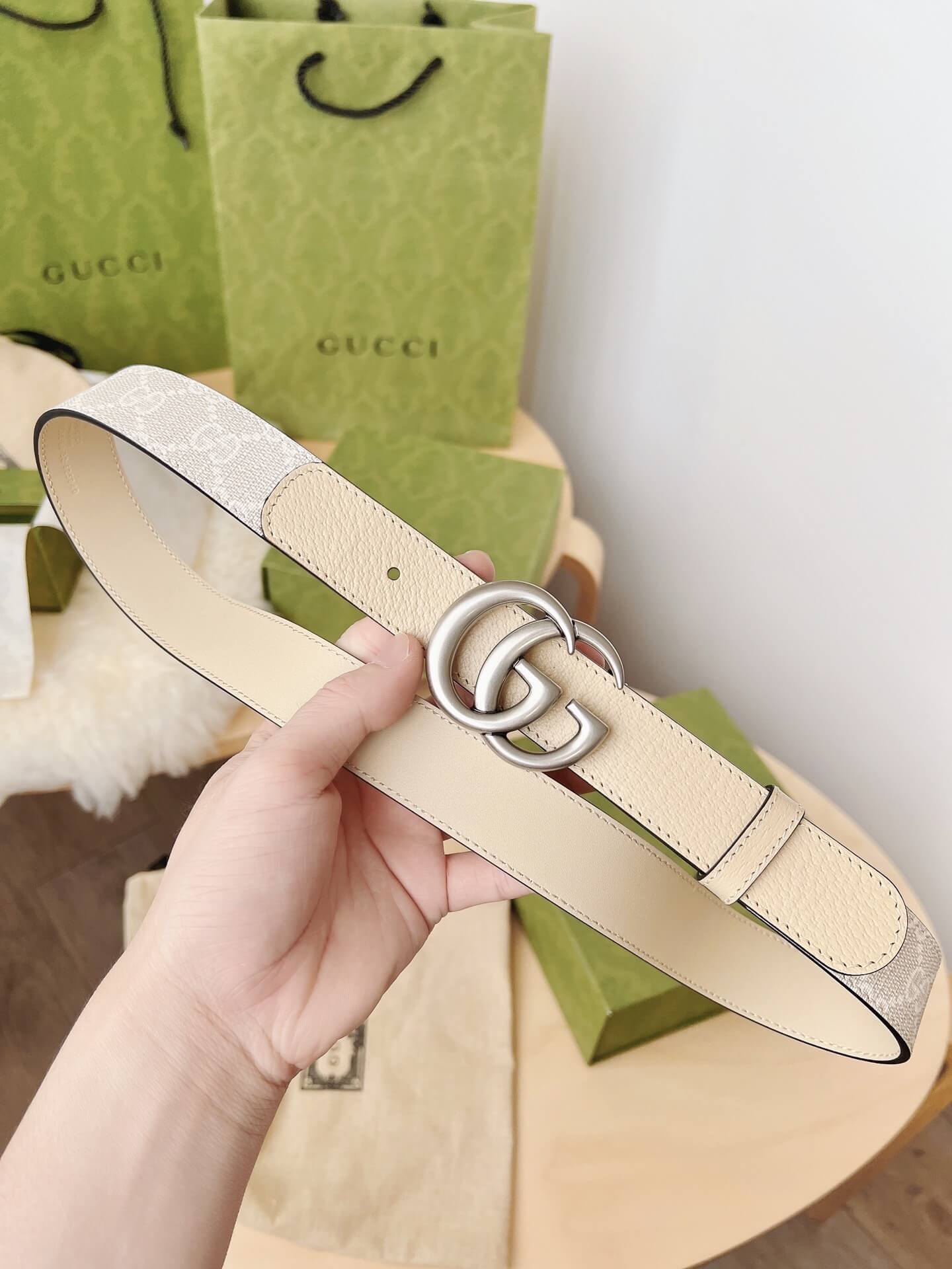 Beige leather belt with silver buckle held by a hand, Gucci branded background
