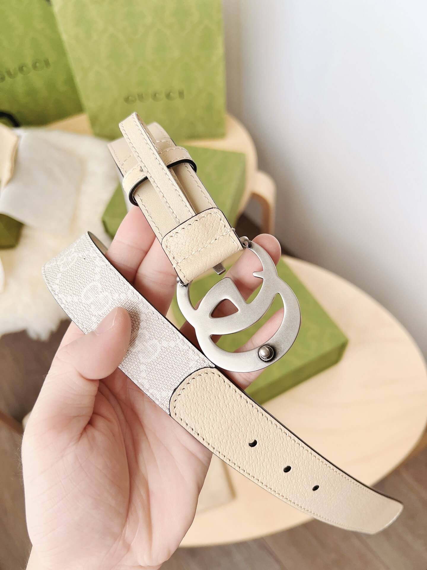 Beige leather belt with a silver buckle held by a hand, Gucci box in the background