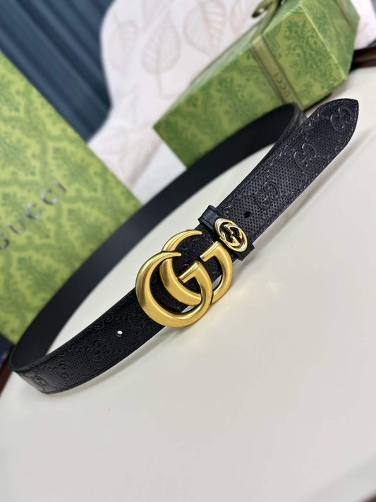 Black Gucci belt with gold logo on a white surface with green packaging in the background.