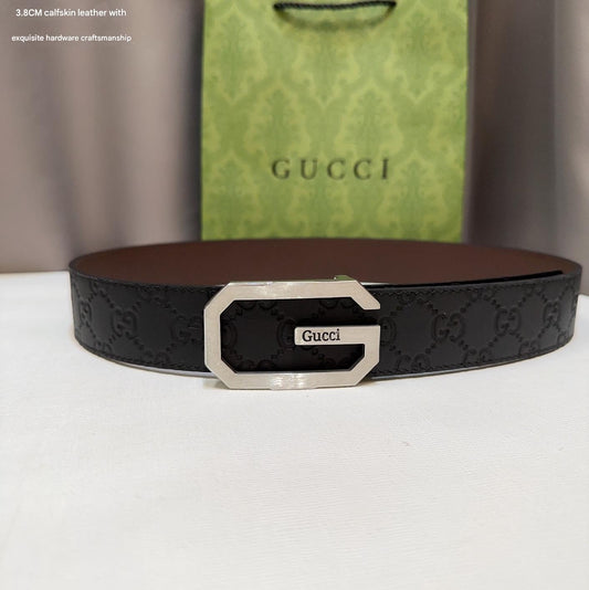 Black Gucci belt with silver buckle on a white surface, with a Gucci green bag in the background.