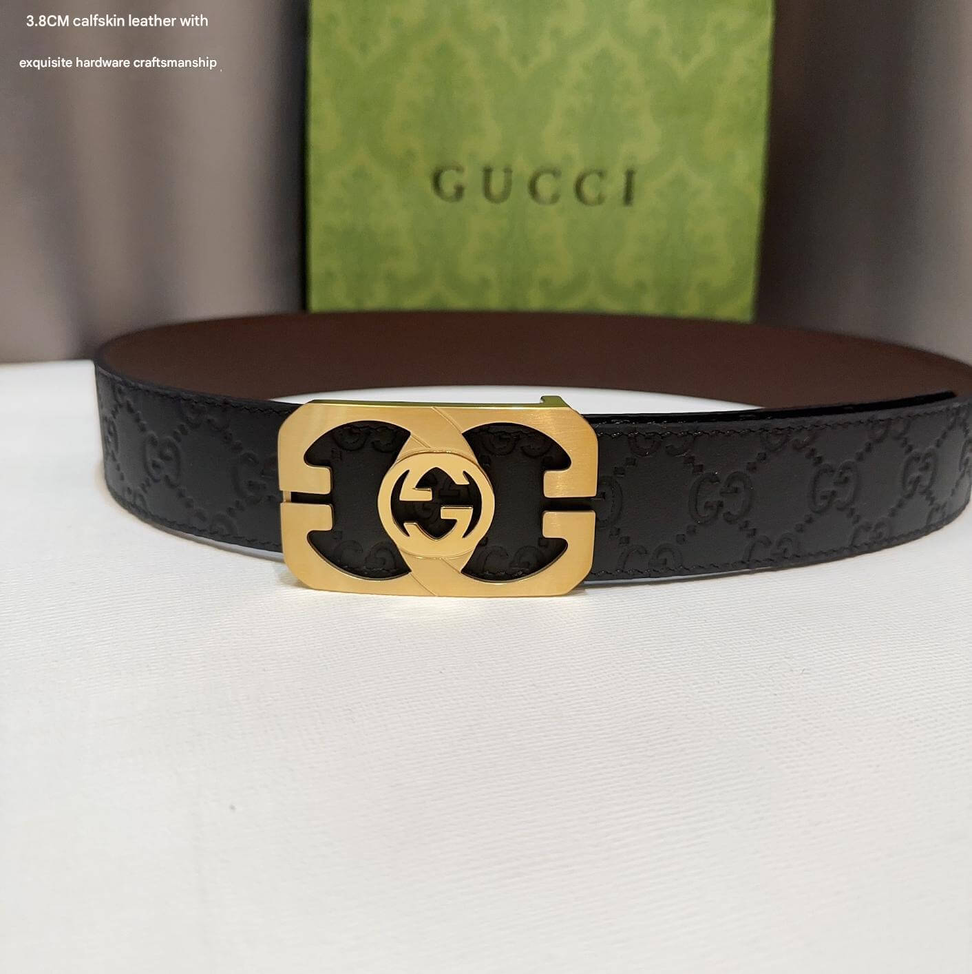 Black Gucci belt with gold buckle on a white surface, Gucci box in the background.