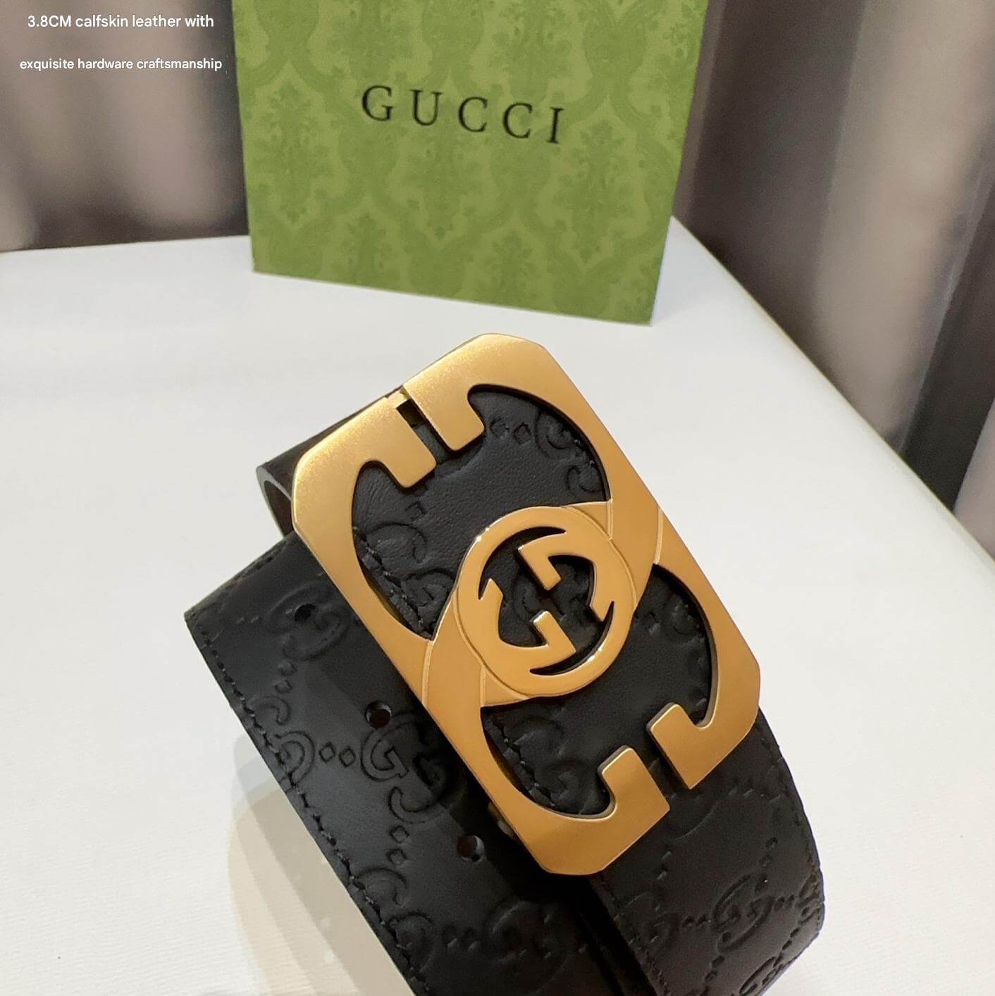 Black Gucci belt with gold buckle on a white surface, Gucci box in the background.