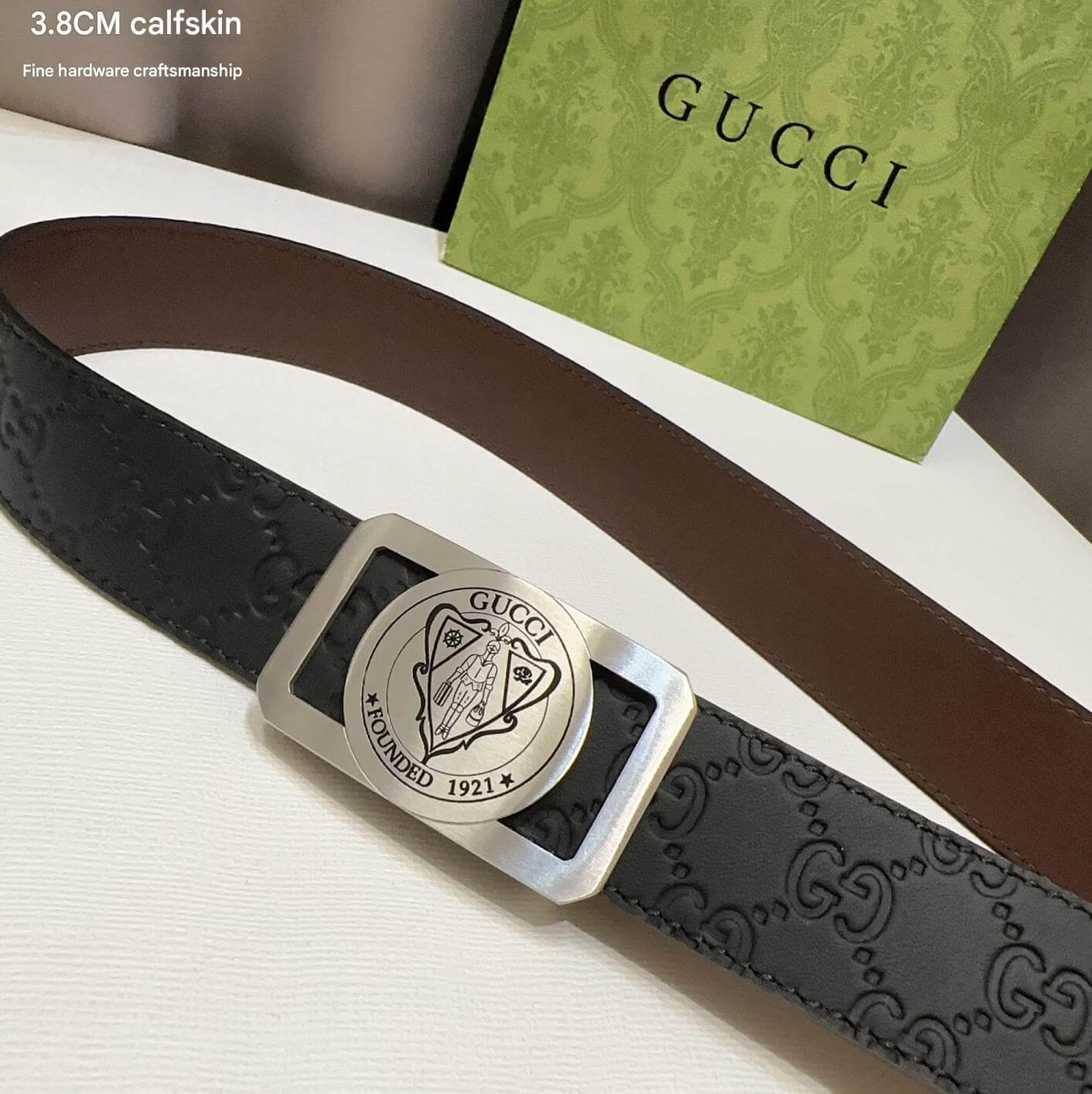 Gucci belt with silver buckle on a white surface with Gucci packaging.