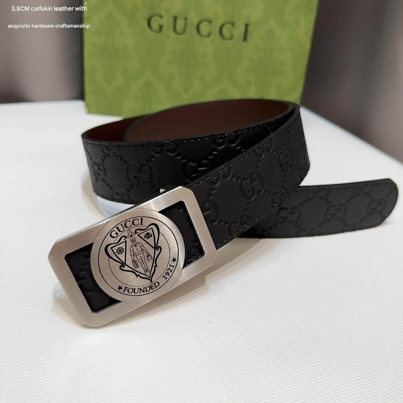 Black Gucci belt with silver buckle on a white surface, Gucci box in the background.