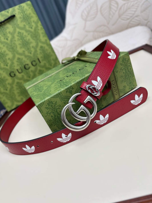 Red Gucci belt with white logo on a green Adidas belt with white logo, both on a white surface.