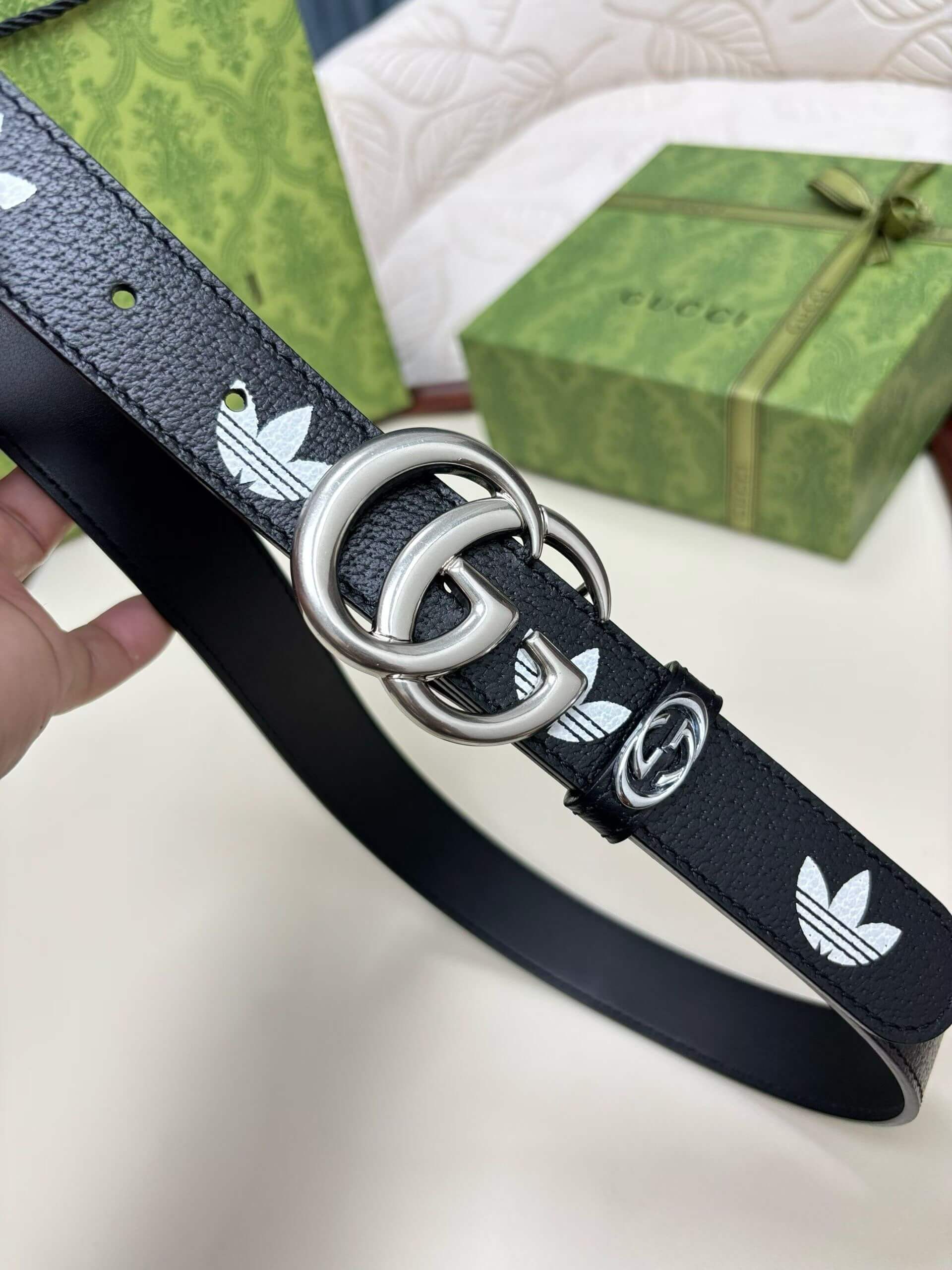 Black belt with silver Adidas logo buckle held by a hand, with a Gucci box in the background.